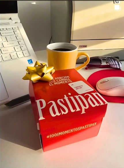 Pieza de Pastipan con una caja de producto y una taza en un escritorio.